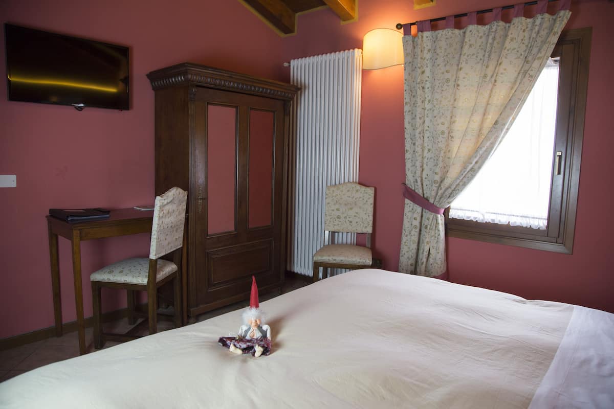 Une chambre à coucher comprenant un lit, une armoire en bois, deux chaises, un bureau, un téléviseur et une fenêtre avec des rideaux.