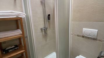 A bathroom with a glass-enclosed shower, a toilet, a sink, and a shelf with towels.
