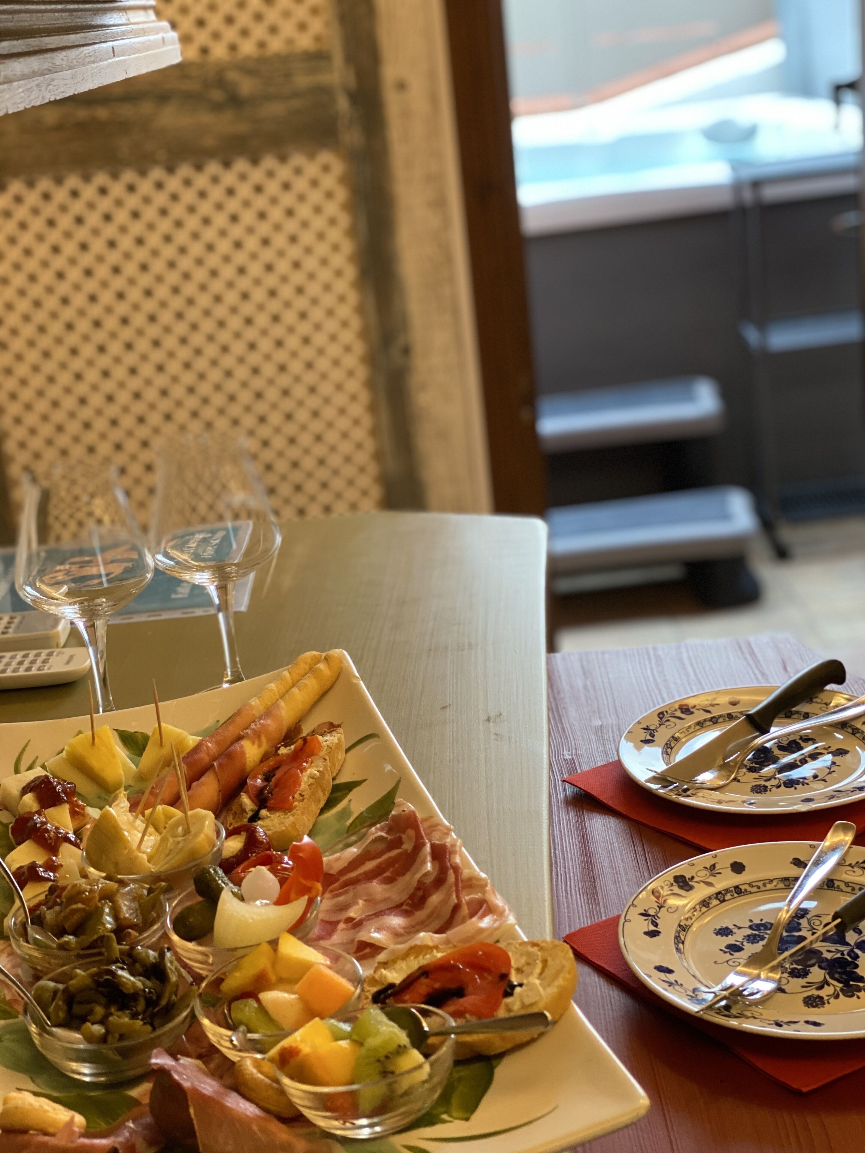 Une table à manger dressée avec une variété d’aliments, notamment du pain, du fromage et de la charcuterie, ainsi que des verres à vin et des couverts.