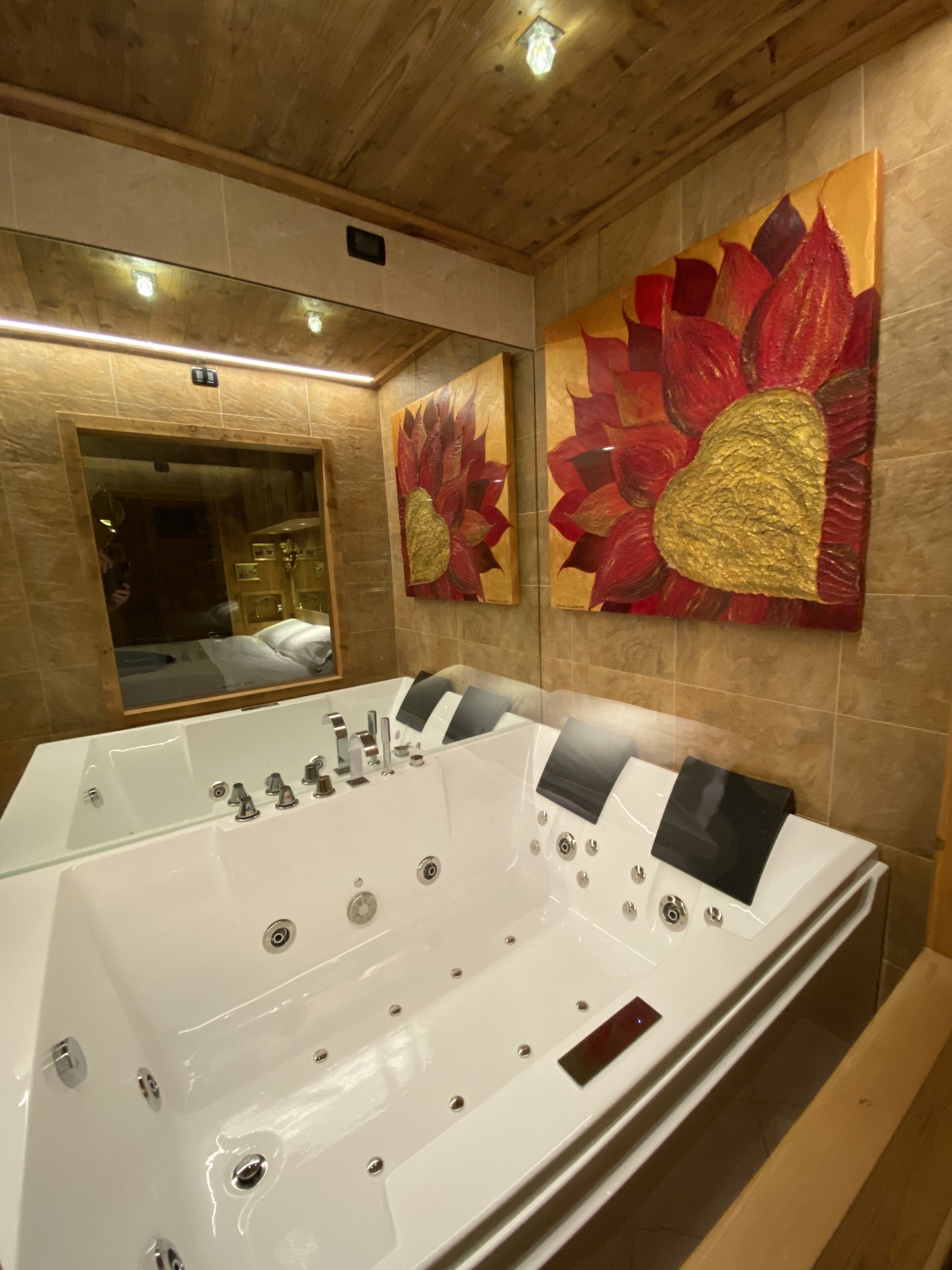 A modern bathroom with a large freestanding bathtub, a mirror, and two large floral paintings on the wall.