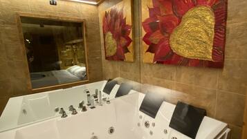 A modern bathroom with a large freestanding bathtub, a mirror, and two large floral paintings on the wall.