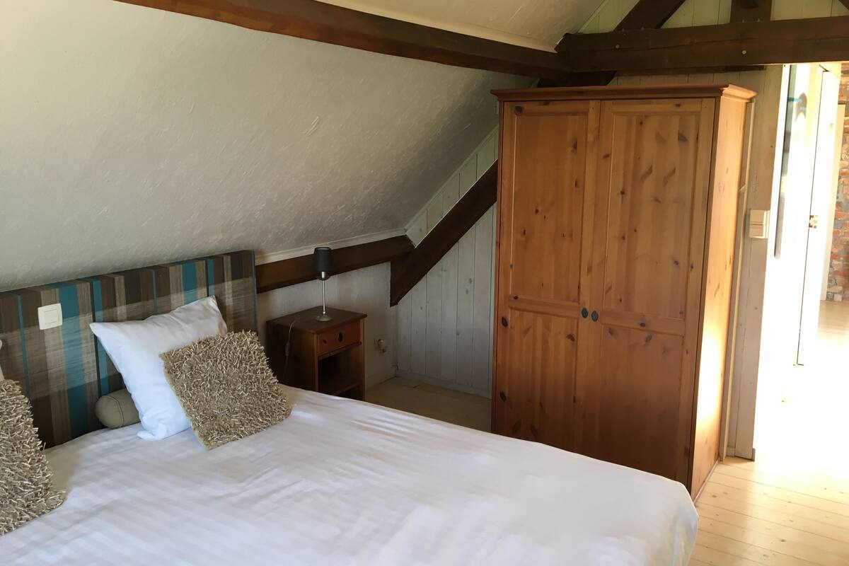 Quarto com cama grande, guarda-roupa de madeira e mesa de cabeceira com abajur.
