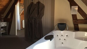 A modern bathroom with a large white bathtub, wooden beams, and a brick wall. - B&B 't Wolvennest (Heuvelland)
