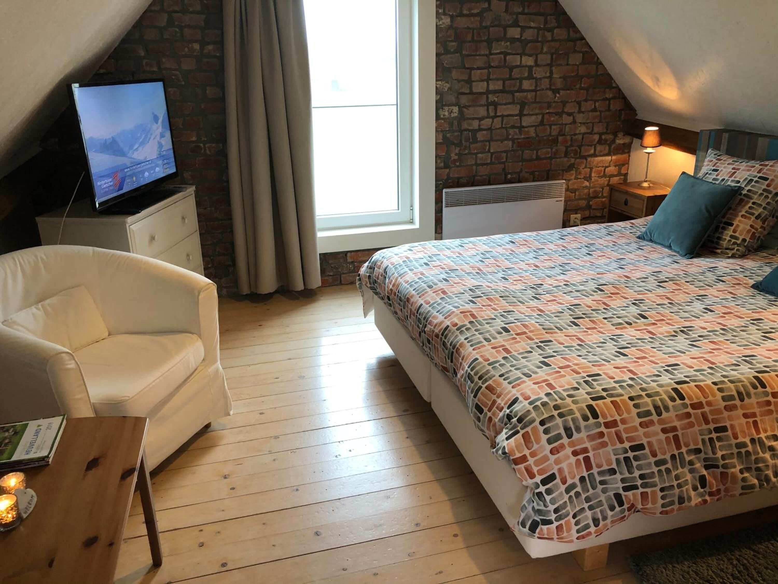 A bedroom with a bed, a television on a nightstand, a chair, and a window with curtains.