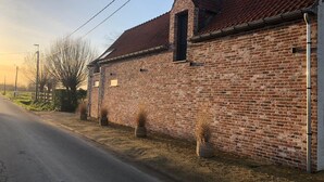 A brick building with a red-tiled roof, a small window, and a utility pole on the right side. - B&B 't Wolvennest (Heuvelland)