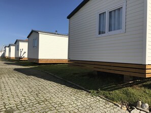 A row of white mobile homes with wooden decks and a paved walkway. - Camping O muiño (Oia)