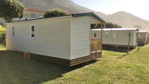 Een gelijkvloerse stacaravan met een veranda en een klein terras, gelegen in een landelijke omgeving met grasvelden en andere vergelijkbare accommodaties.