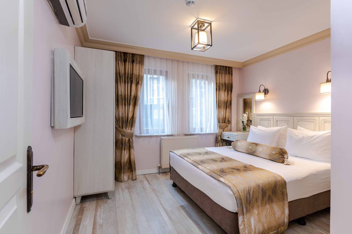 Habitación de hotel con cama, mesita de noche, espejo, ventana con cortinas y aire acondicionado instalado en la pared.