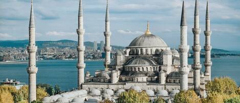 A historic building with multiple minarets and domes, surrounded by trees and a body of water.
