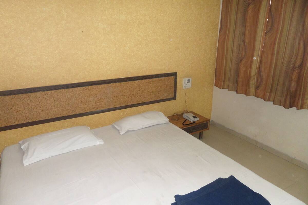 A hotel room with a single bed, a nightstand, a power outlet, and a window with curtains.