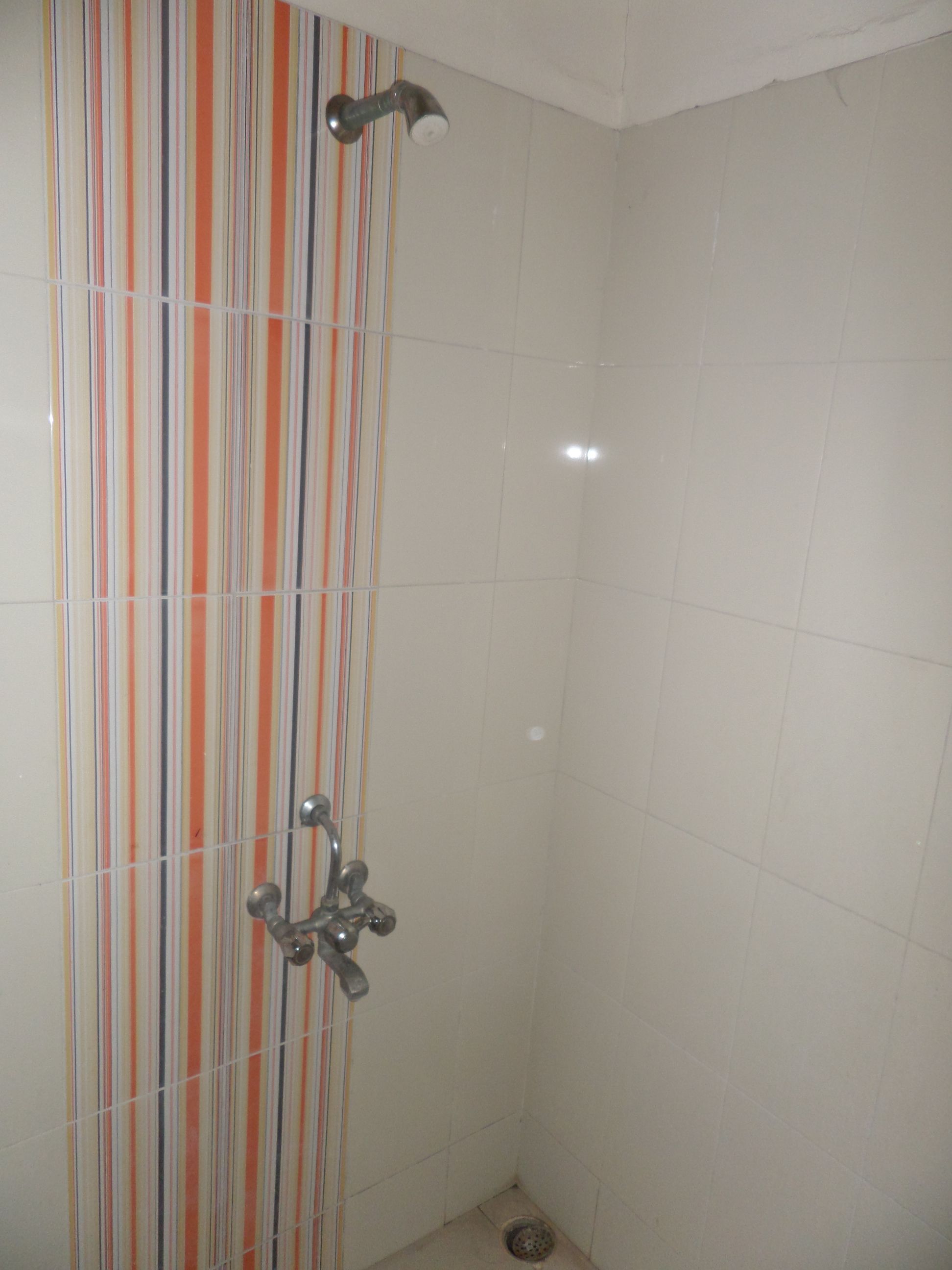 A shower with a vertical striped tile wall and a metal showerhead.