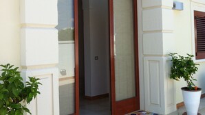 A building entrance with a glass door, a tiled entrance area, and two potted plants. - Affittacamere Torre Lapillo (Porto Cesareo)