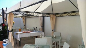 An outdoor patio with a table set for dining, surrounded by wicker chairs and covered by a canopy. - Affittacamere Torre Lapillo (Porto Cesareo)