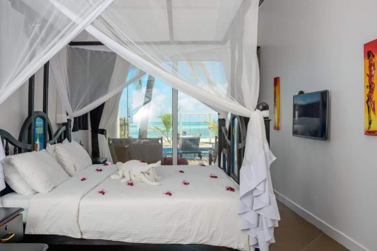 Ein Schlafzimmer mit Bett, weißen Vorhängen, Meerblick und einem Sessel.