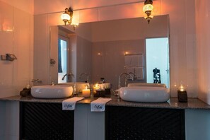 Une salle de bain avec deux lavabos, un miroir et un meuble-lavabo. On y trouve des bougies sur le comptoir et un porte-serviettes au-dessus du miroir.