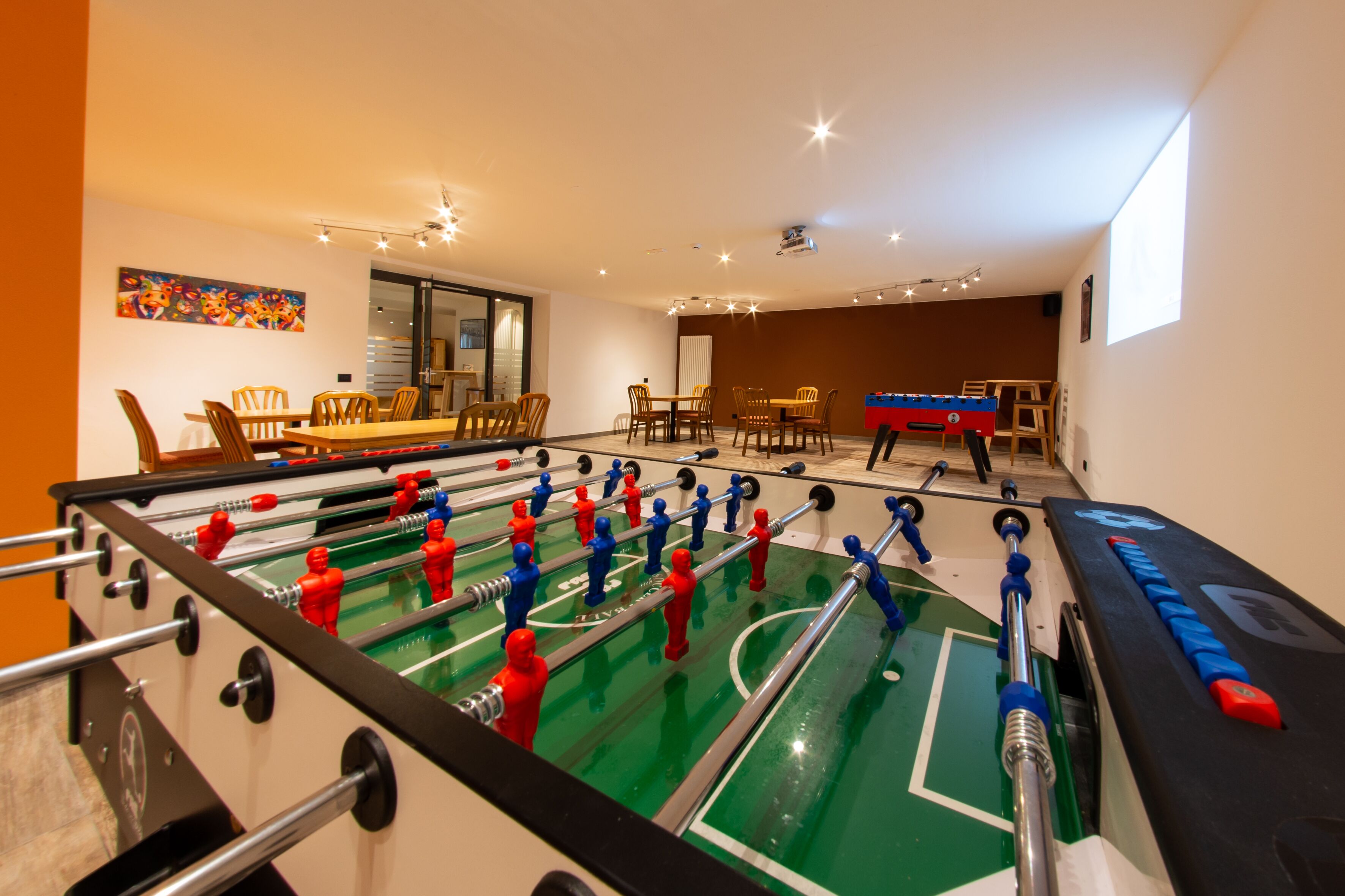 A room with a foosball table, a dining table with chairs, and a large window providing natural light.