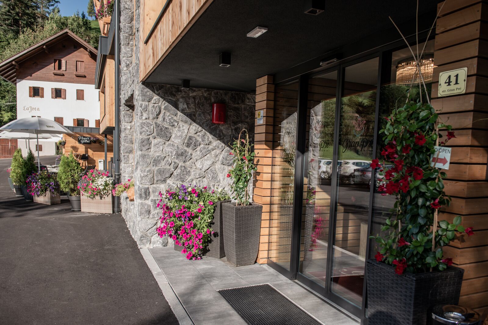 A hotel entrance with stone facade, large windows, and outdoor seating with potted plants.