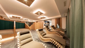 A modern spa area with multiple massage chairs, a wooden staircase, and a view into a kitchen area. - Hotel Gran Pre (Marebbe)