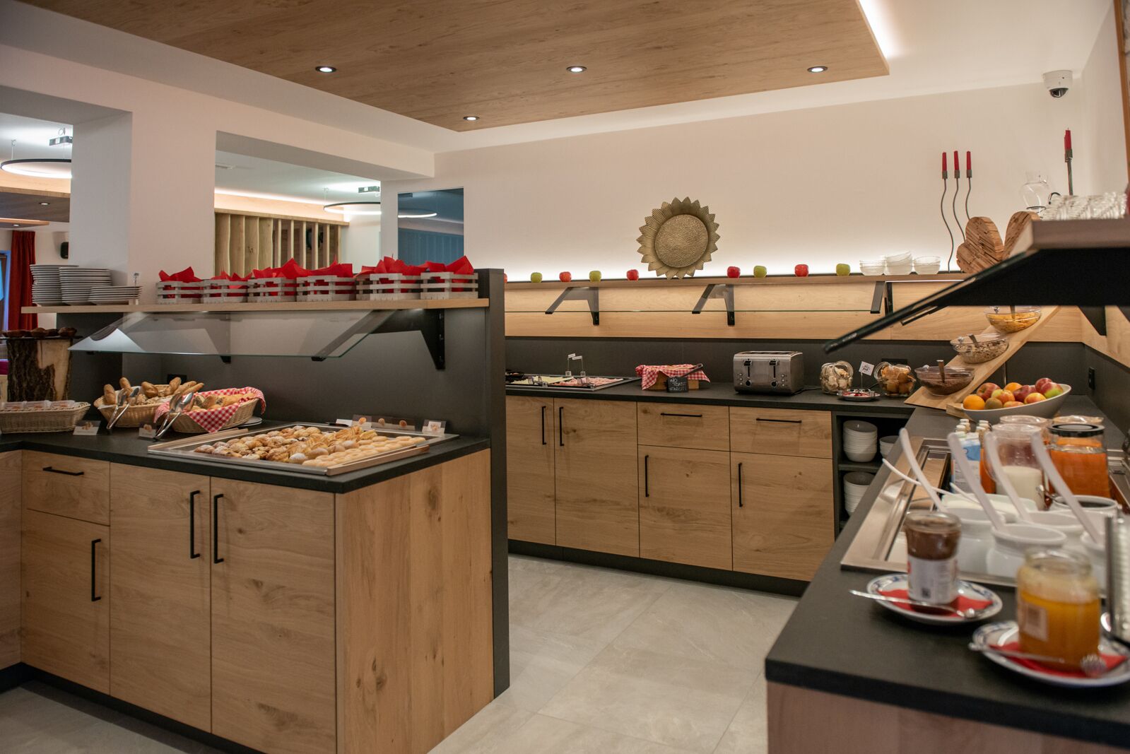 Una cocina moderna con armarios de madera, un mostrador de buffet con diversas opciones de comida y un adorno con forma de sol en la pared.