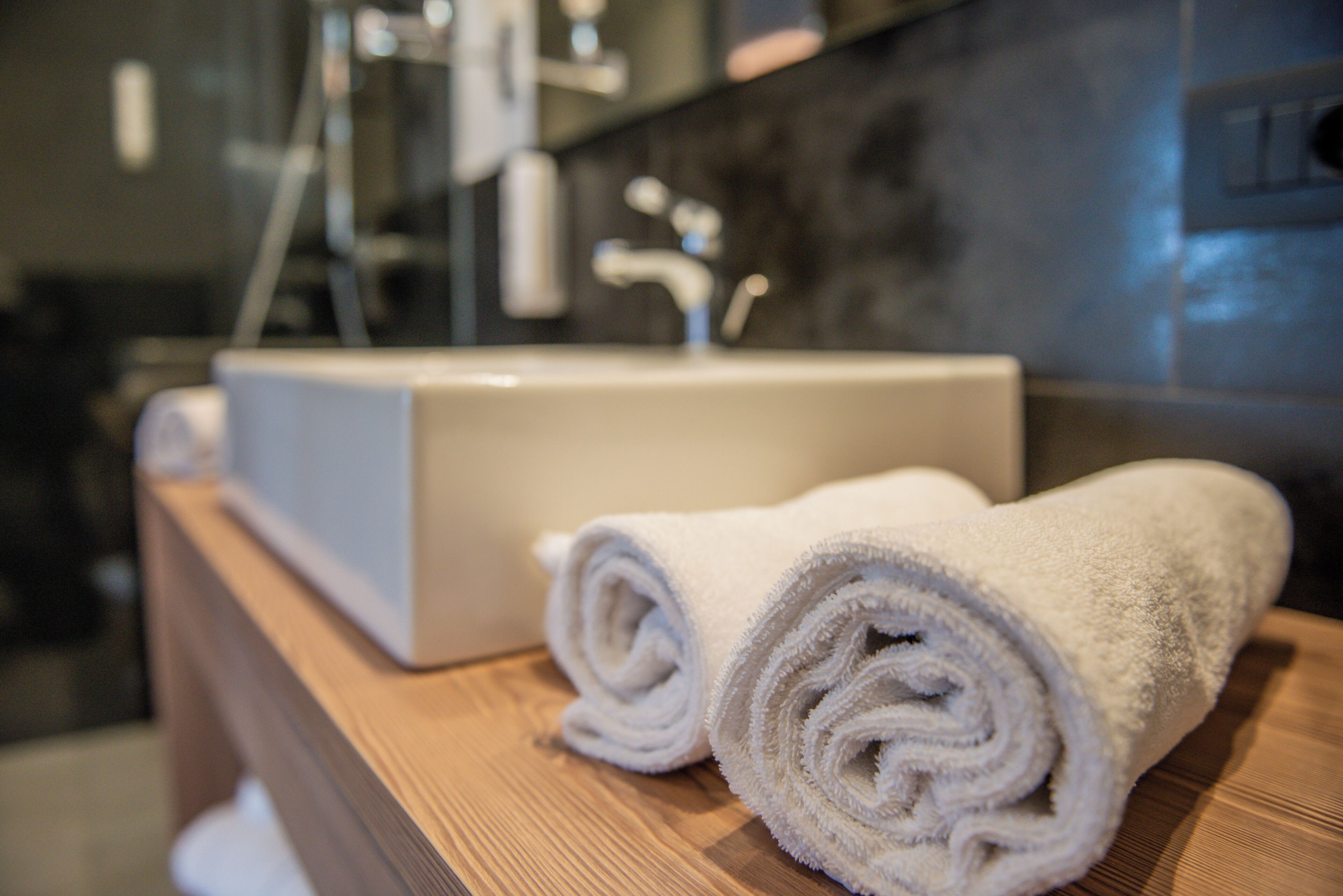 Ein Badezimmer mit einem Holzmöbelkorpus, einem weißen Waschbecken und zwei aufgerollten Handtüchern.