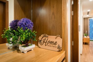 A wooden sign with "Home Sweet Home" written on it, placed on a wooden table next to two potted plants with green leaves and purple flowers. - Park Hill No1 Apartment (Hanoi)