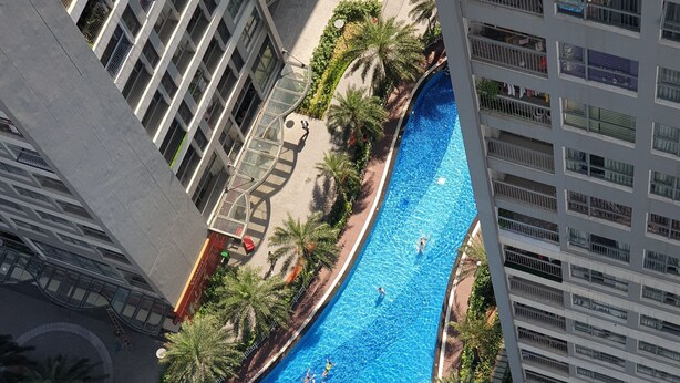 A large, curved swimming pool surrounded by palm trees and modern buildings. - Park Hill No1 Apartment (Hanoi)