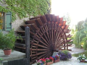 Ein großes, aus Holz gefertigtes Wasserrad mit rustikalem Charme, umgeben von Topfpflanzen und Blumen.