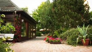 Un chemin pavé de briques mène à un bâtiment en bois doté de grandes fenêtres et agrémenté d’une composition florale suspendue.