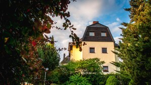 Une maison à deux étages, dotée d’un toit en pente, entourée d’une végétation luxuriante et d’une pelouse bien entretenue.