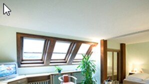 Une pièce comprenant un bureau, une chaise, une table avec une plante, un radiateur et une fenêtre.