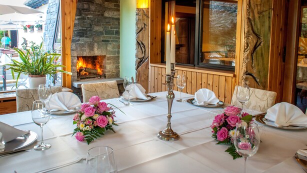 Une table à manger dressée pour quatre personnes, avec des nappes blanches, des centres de table floraux roses et des bougeoirs.