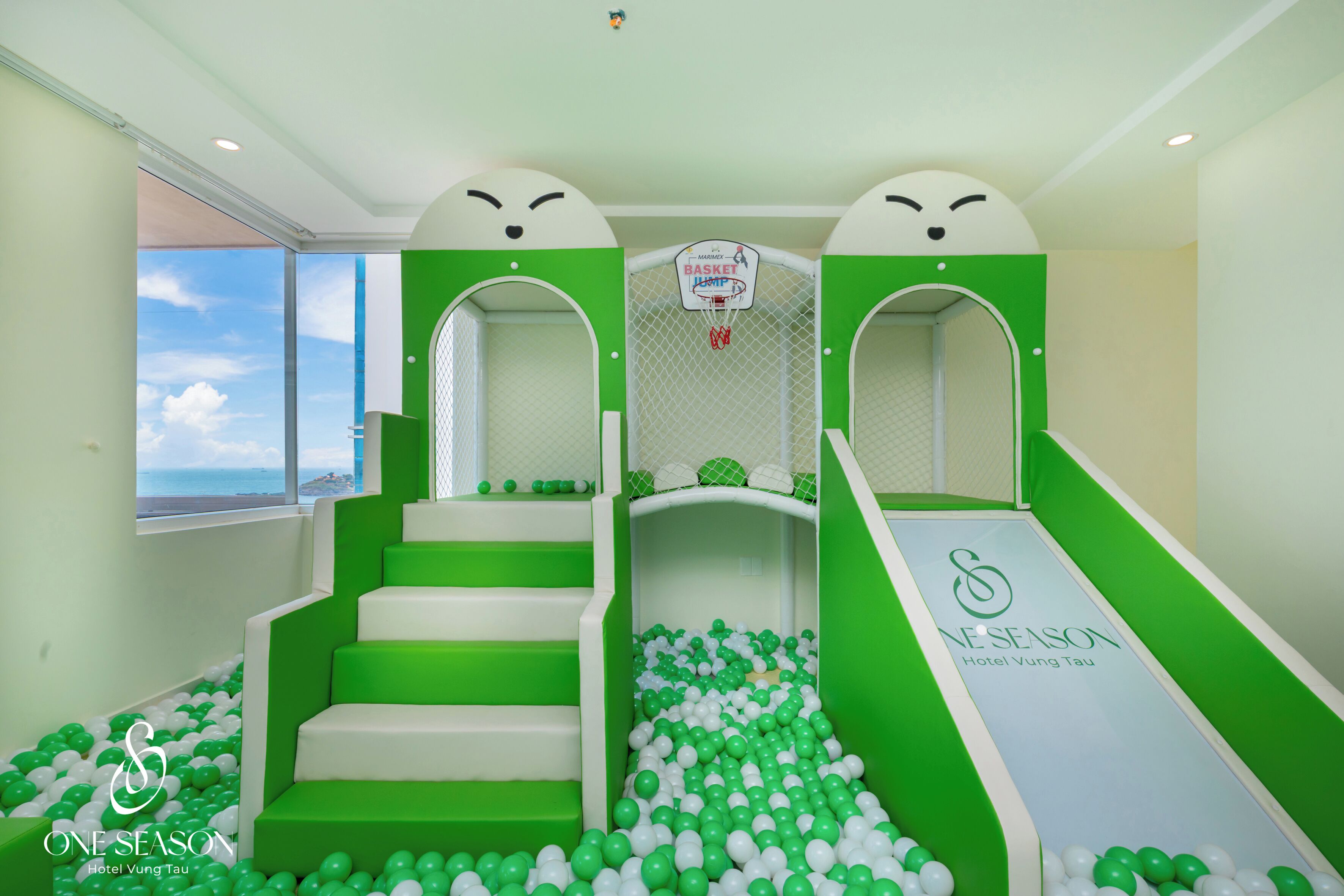 Ein Kinderspielbereich mit Basketballkorb, grün-weißen Treppen und einer Bällecke.