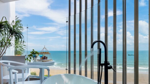 A modern bathroom with a large bathtub, a small table with chairs, and a view of the beach. -  One Season Boutique Hotel Vung Tau - Beachfront (Ho Chi Minh City)