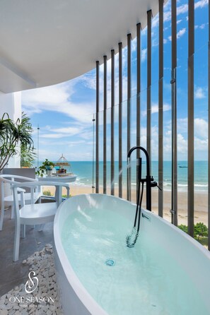Ein modernes Badezimmer mit einer großen Badewanne, einem kleinen Tisch mit Stühlen und Blick auf den Strand.