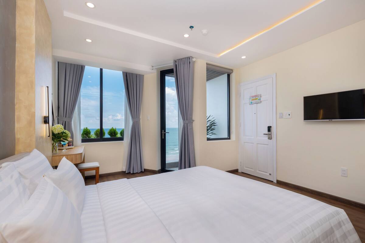 Ein modernes Hotelzimmer mit einem großen Bett, einem Schreibtisch, einem Sessel, einem Fernseher und Meerblick.