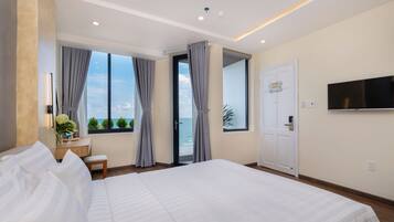 A modern hotel room with a large bed, a desk, a chair, a TV, and a view of the sea.