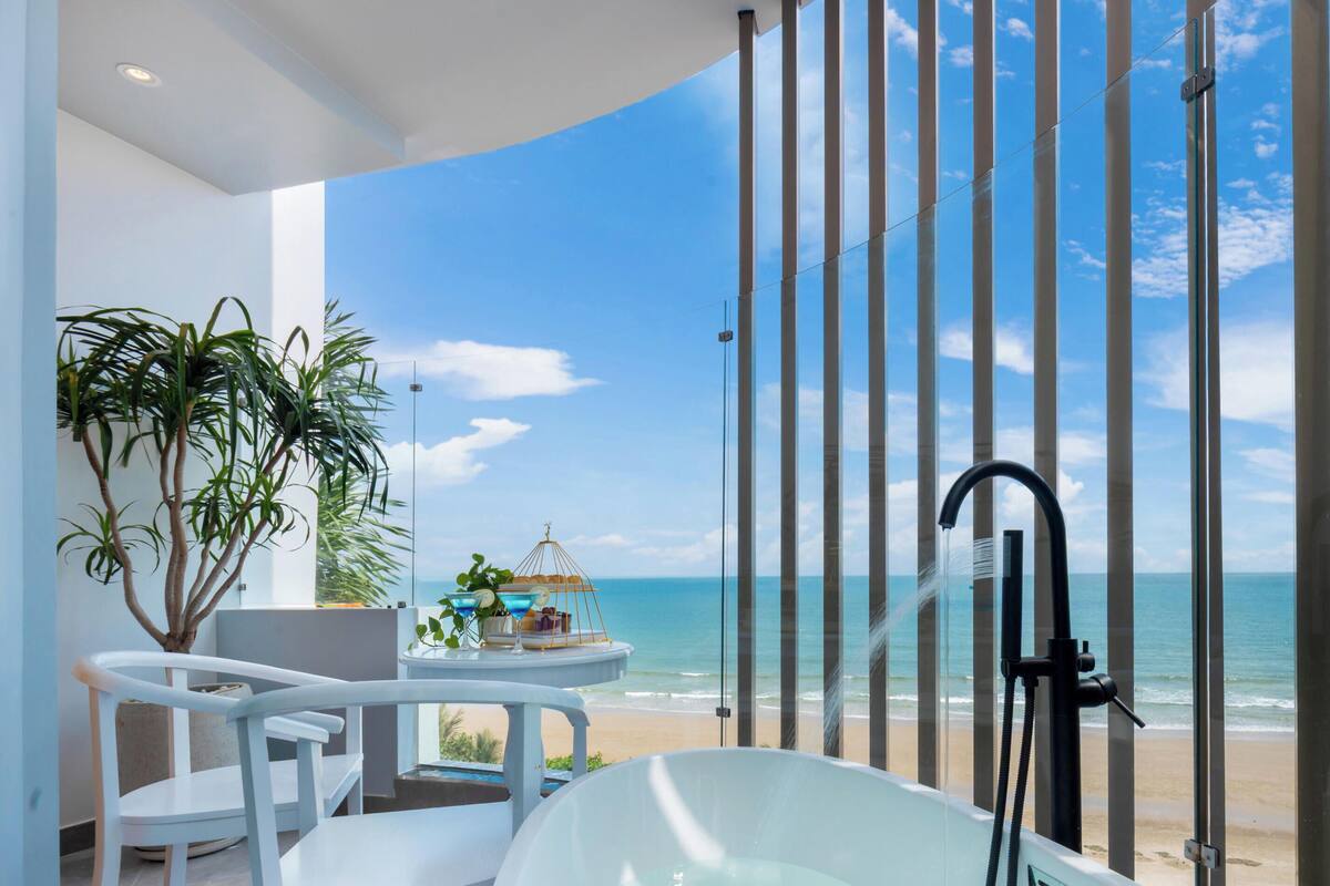 Ein modernes Badezimmer mit einer großen Badewanne, einem kleinen Tisch mit Stühlen und Blick auf den Strand.