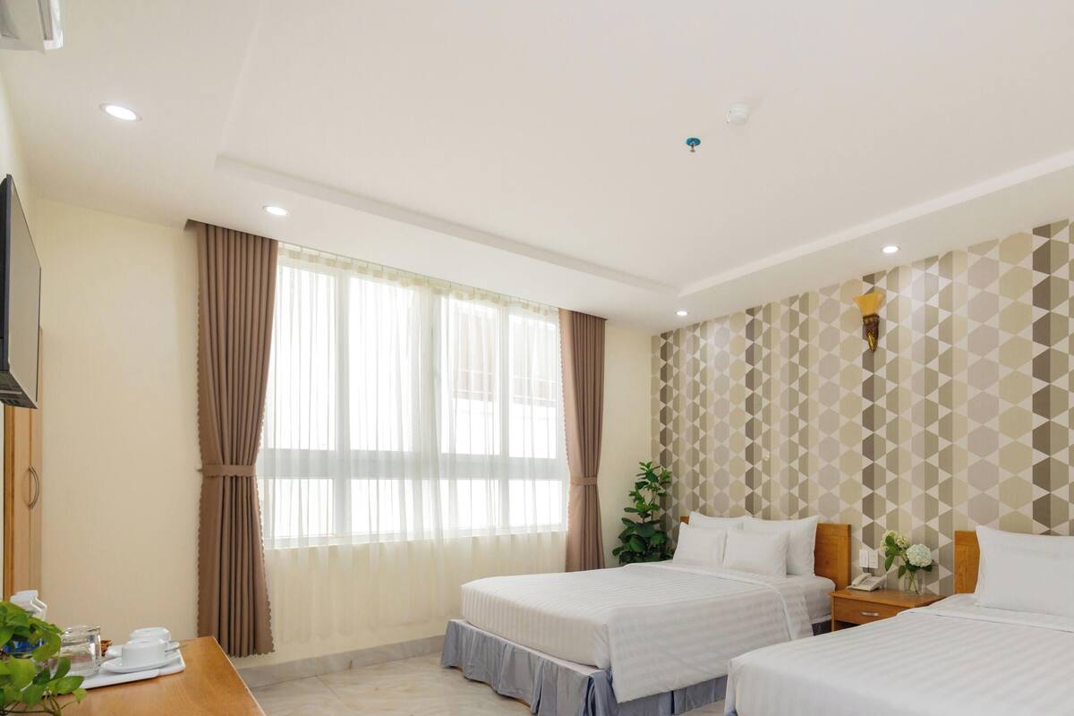 Ein Hotelzimmer mit zwei Betten, einem Schreibtisch und einem großen Fenster mit Vorhängen.