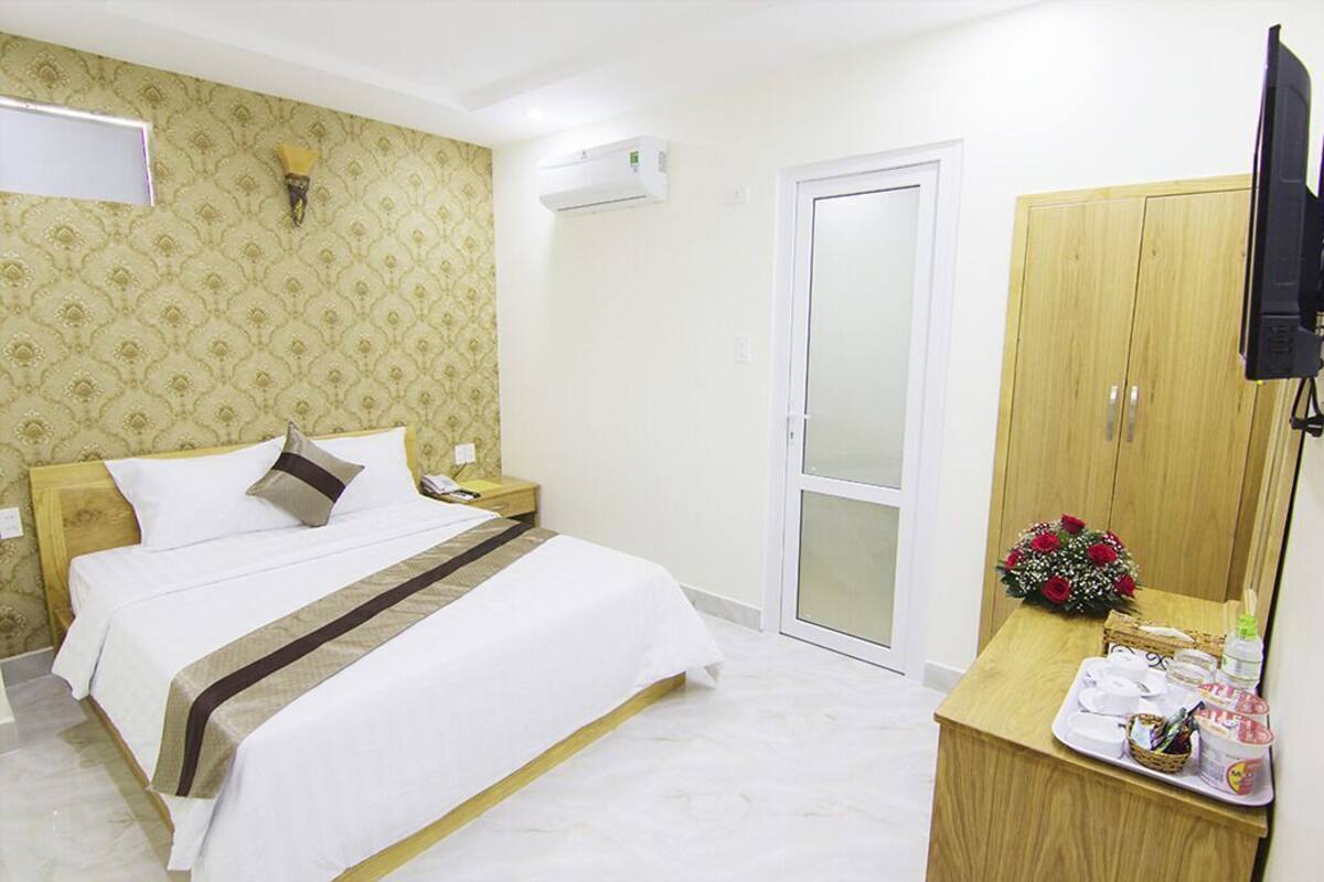 Ein Hotelzimmer mit einem Bett, einem Holzschrank, einem Fernseher und einem kleinen Tisch mit einem Blumenstrauß.