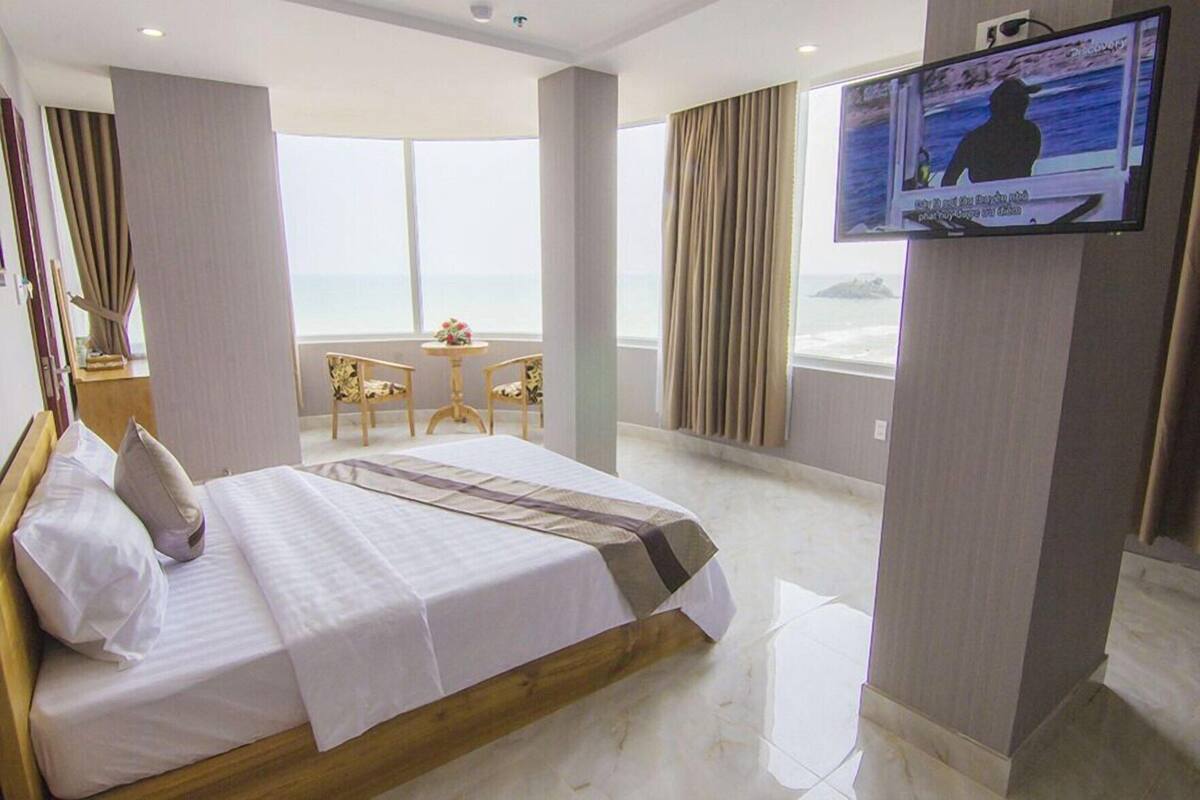 Ein Hotelzimmer mit Bett, Fernseher, Balkon und Meerblick.