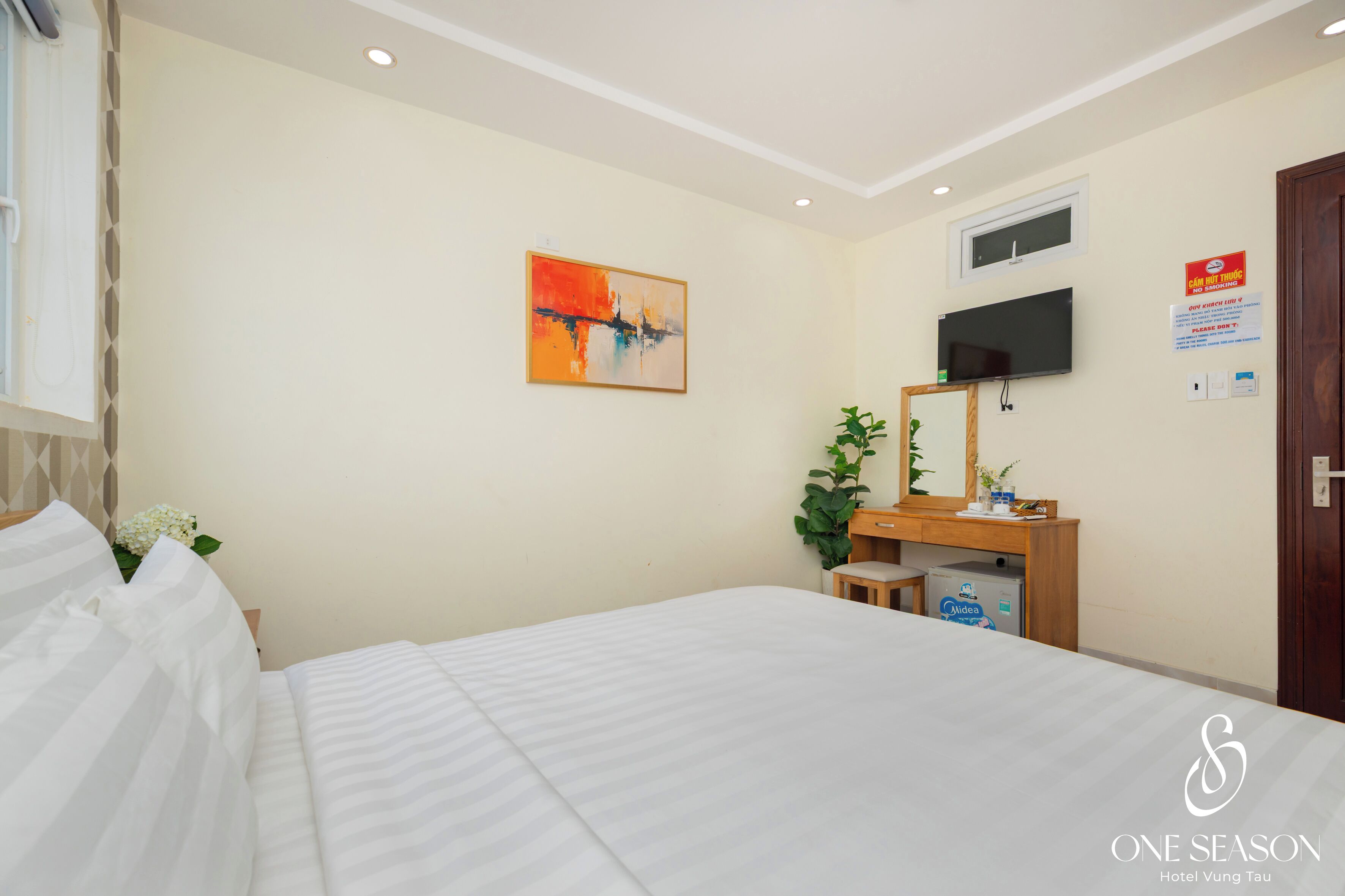A hotel room with a bed, a desk with a mirror, a television, and a painting on the wall.