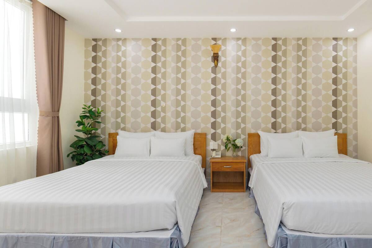 Ein Hotelzimmer mit zwei Betten, einem Nachttisch, einer Topfpflanze und einer Wand mit geometrischem Muster.