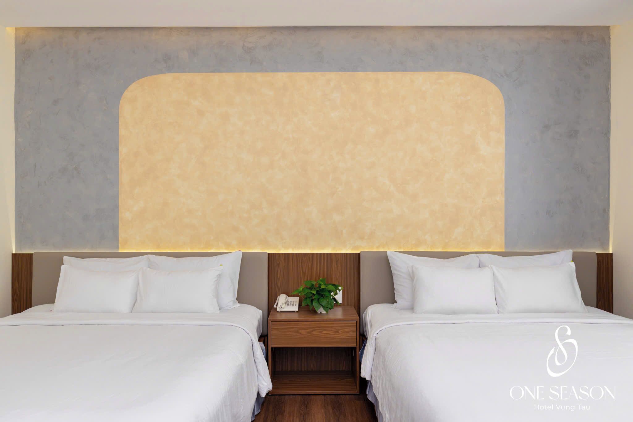 A hotel room with two beds, a wooden nightstand with a phone and a plant, and a large abstract wall design.