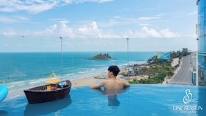 A man relaxing in an infinity pool with a view of the beach and ocean. -  One Season Boutique Hotel Vung Tau - Beachfront (Ho Chi Minh City)
