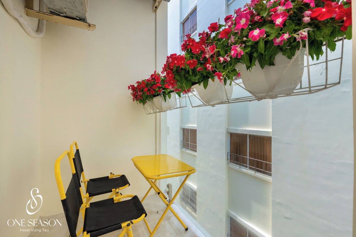 Ein gelber Klapptisch und zwei Stühle in einer Ecke, über ihnen eine hängende Blumenampel.