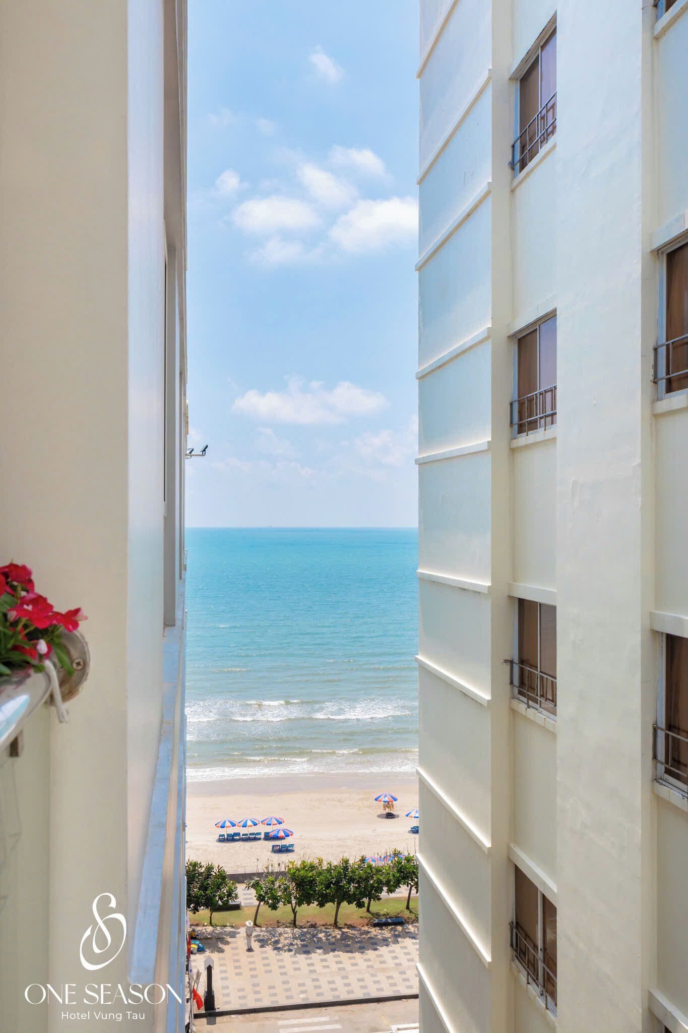 A balcony with a view of the beach, hotel building, and a clear sky.