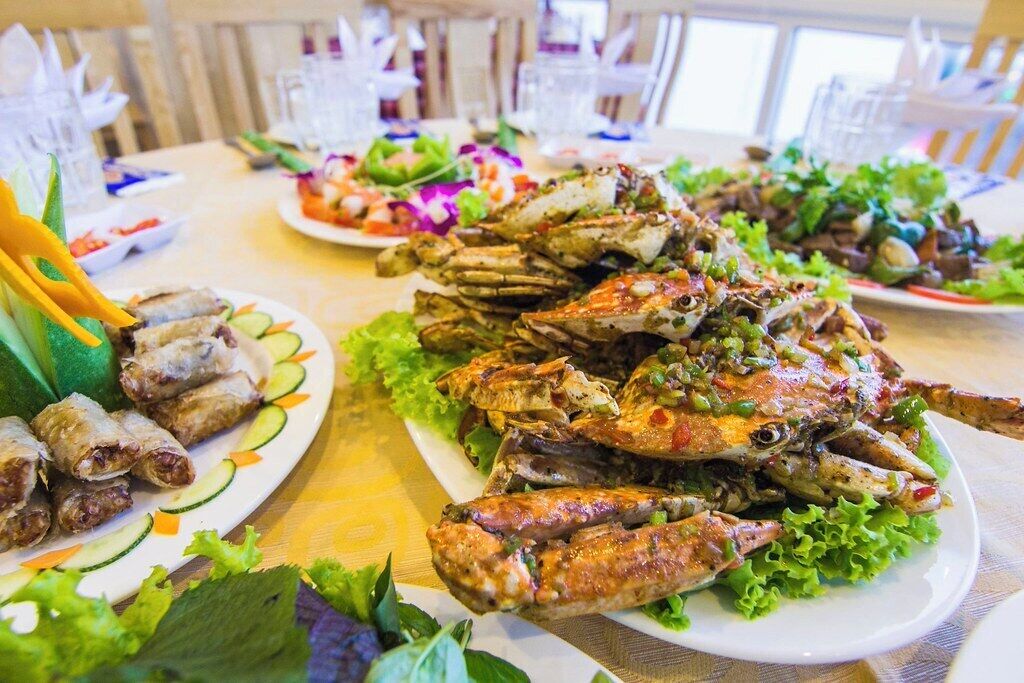 A table set with various dishes including grilled crabs and spring rolls, surrounded by plates of salad and other appetizers.