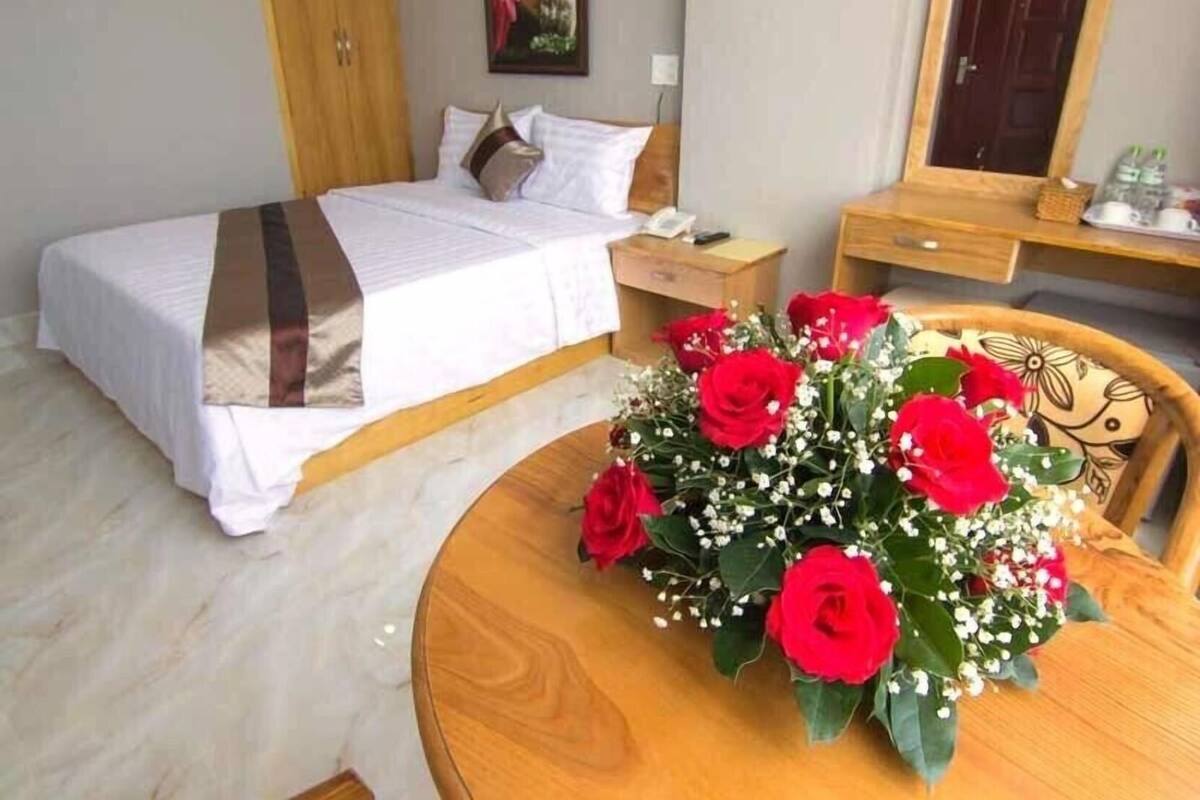 Ein Hotelzimmer mit einem Bett, einem Nachttisch und einem runden Holztisch mit Blumenarrangement.