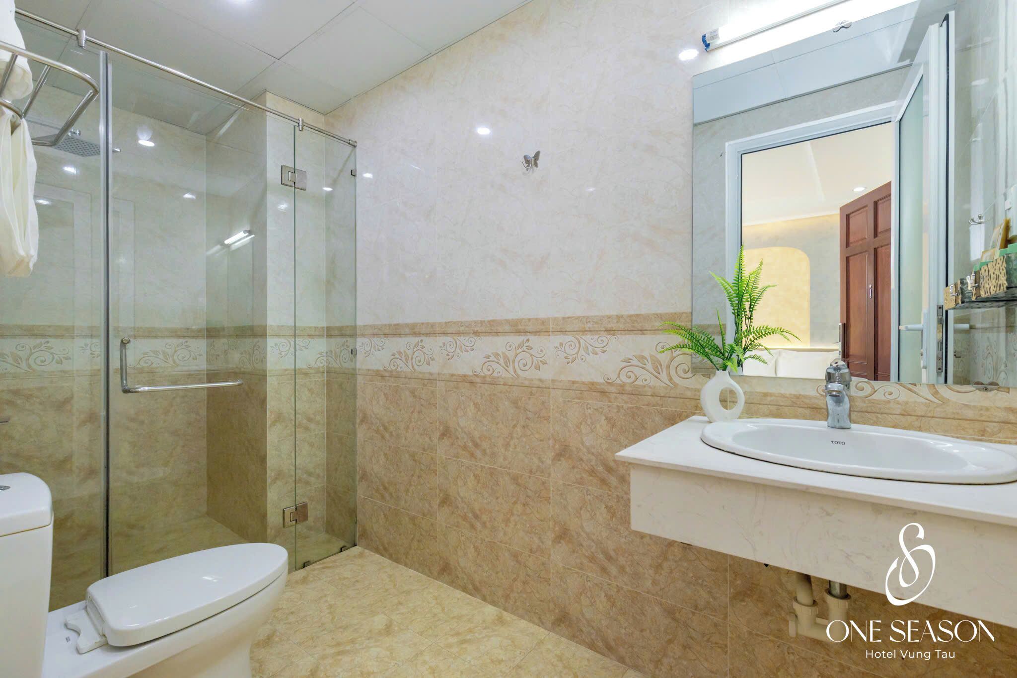 A bathroom with a glass-enclosed shower, a toilet, a sink with a mirror, and a decorative plant.