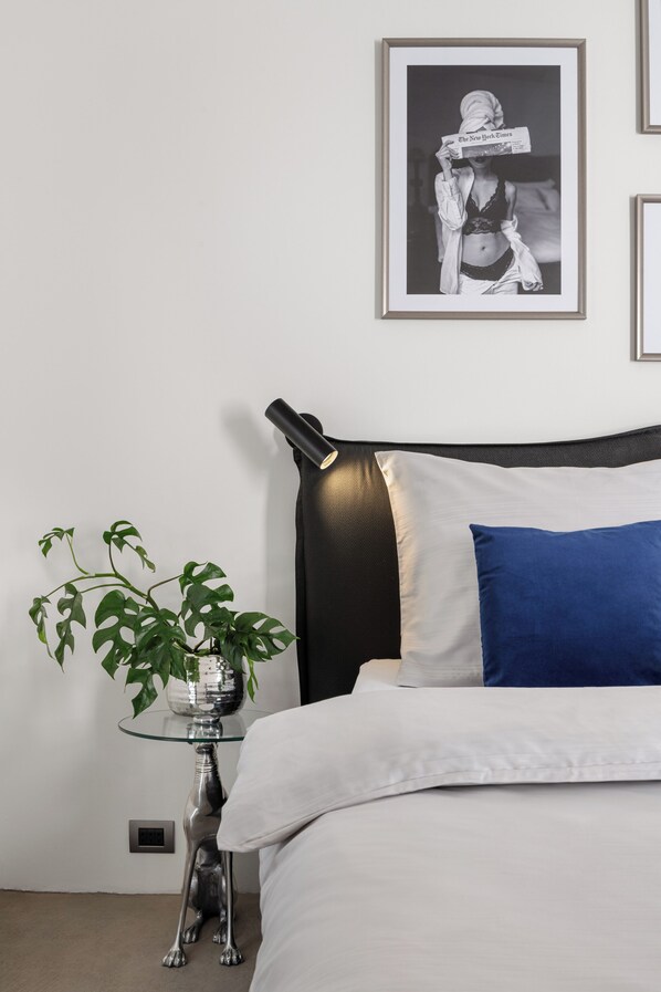 A neatly arranged bedroom with a bed, a framed picture on the wall, a small round table with a plant, and a unique dog-shaped side table.